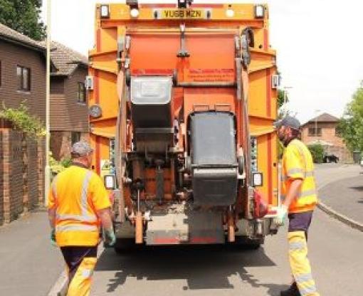 Two men in orange high vis collecting black wheelie bins with an orange bin collection lorry