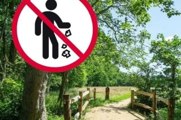 A parth leading through a wooded area with blue sky. An anti-litter sign is on top of the imagen