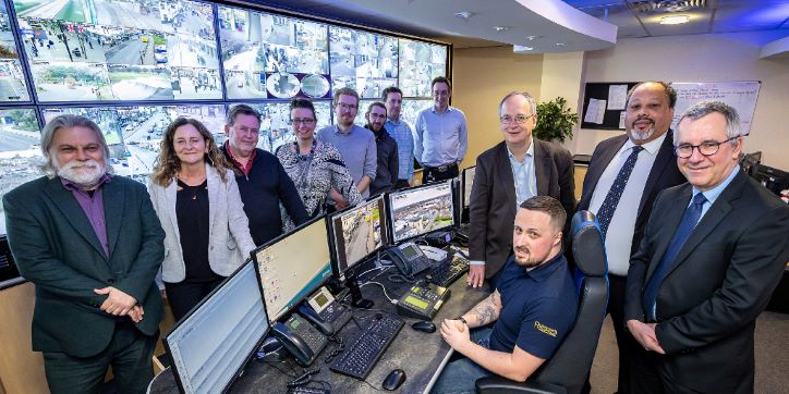 Councillor David Neighbour, Leader of Hart District Council, and Councillor Stuart Bailey, portfolio holder for community at Hart District Council, at the Runnymede CCTV control centre with a bank of monitors and group of councillors and council officers
