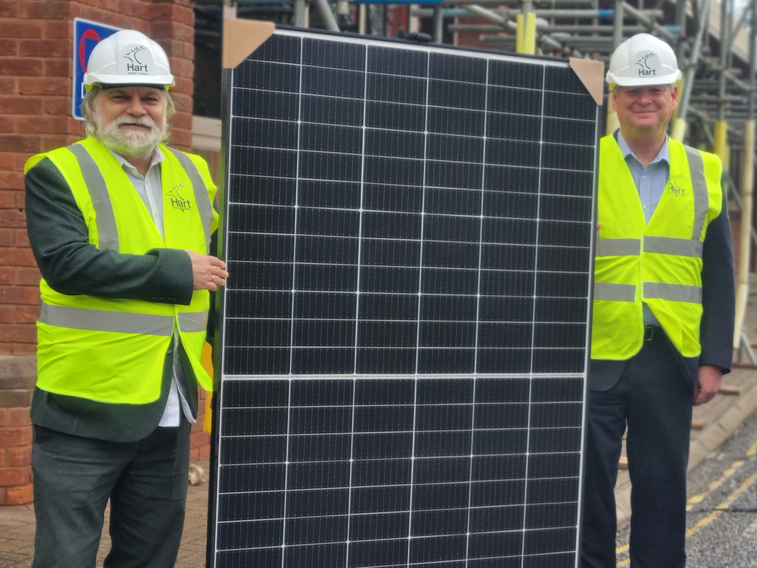 Two men in hard hats and hi viz jackets holding solar panel