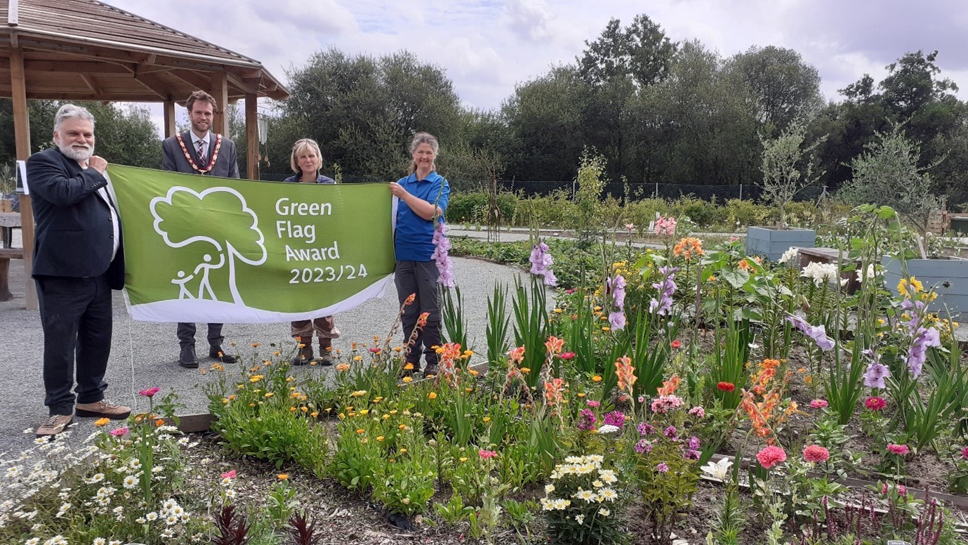 Leader of the Council Councillor David Neighbour, Hart District Council Chairman Councillor Peter Wildsmith, Hart Voluntary Action Wellbeing Projects Officer Amanda Slater and Hart Countryside Ranger Sarah Leedham at Edenbrook Country Park with the Green Flag Award flag