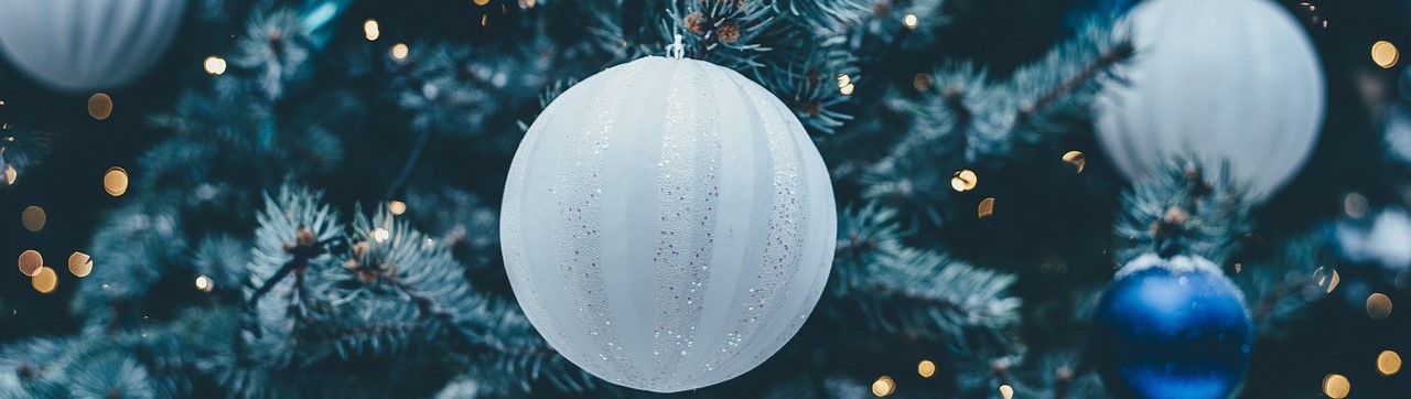 White and blue Christmas baubles on a tree with fairy lights