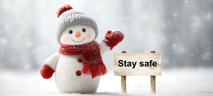 Snowman wearing red hat, gloves and scarf beside a noticeboard with stay safe written on it