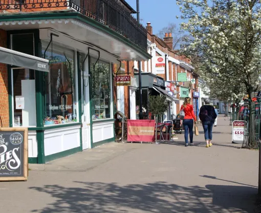 Two people walking past shops on Hartley Wintney high street