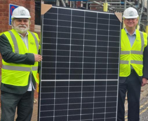 Dave Neighbour, leader of the Council, and chief executive Daryl Phillips, with one of the solar panels. They are wearing hard hats and high-visibility jackets.