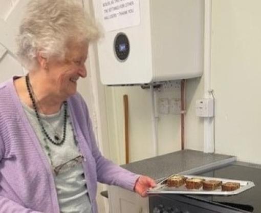 Older woman holding a tray of cakes beside a new oven