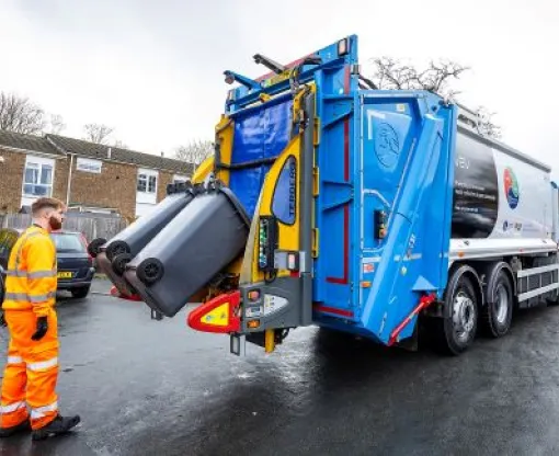 Man in an orange high viz suit collects black bins in the zero-emission bin truck