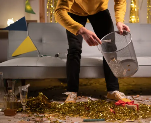 Man holding wastepaper basket and sweeping up tinsel and glitter