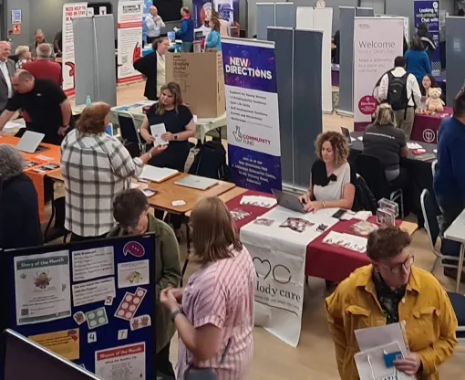 A hall with groups of people talking to each other with stands and posters