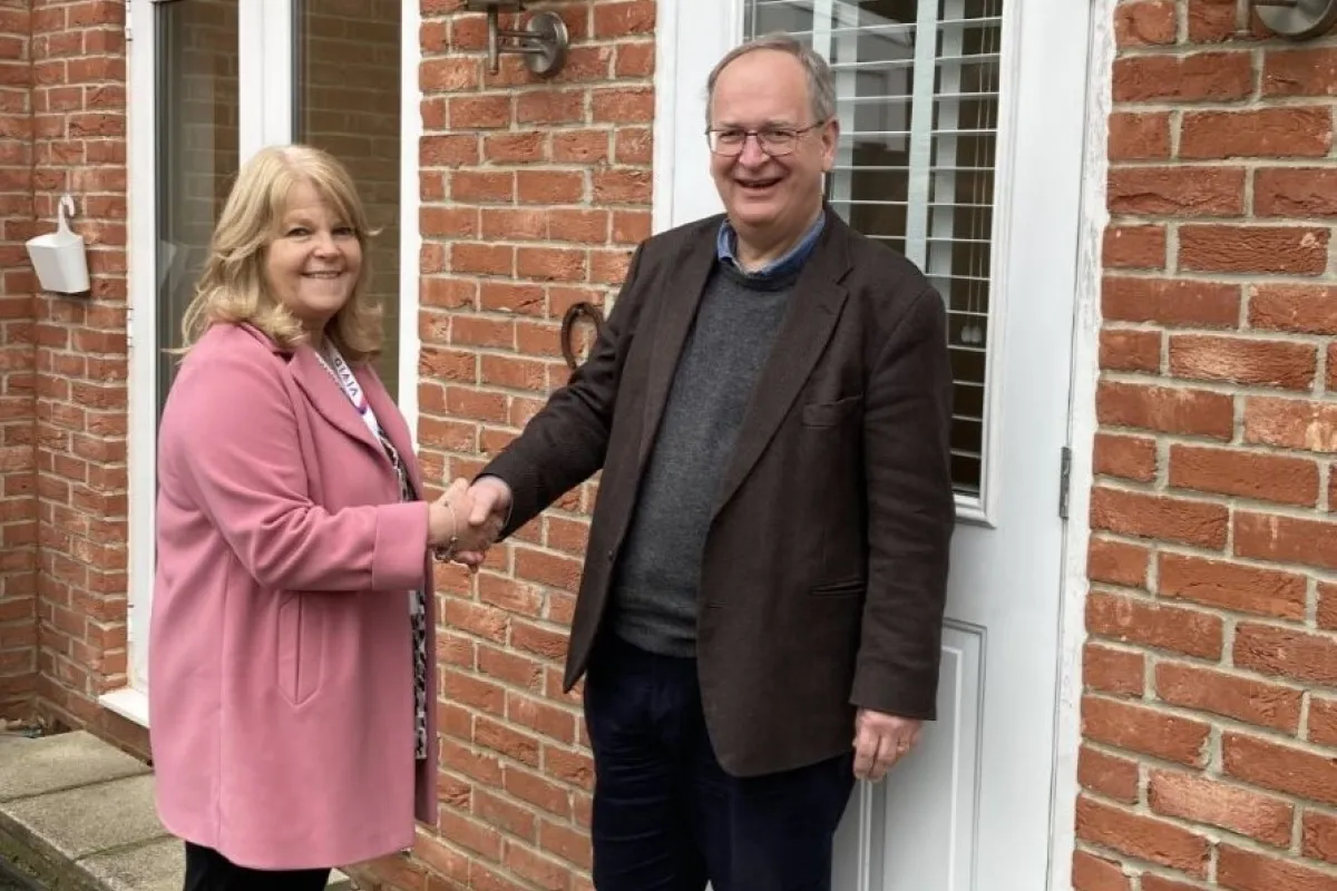 A man and a woman shaking hands outside a red brick house with a white door