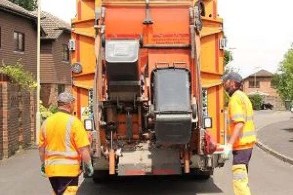 Two men in orange high vis collecting black wheelie bins with an orange bin collection lorry