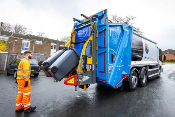 Man in an orange high viz suit collects black bins in the zero-emission bin truck