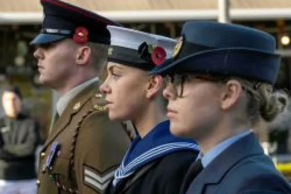 A soldier, sailor and RAF personnel in uniform and standing in a line with red poppies attached to hats
