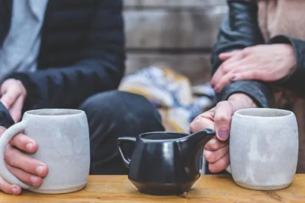 Two people having a hot drink with hands around two mugs and a jug