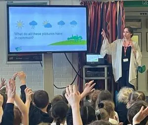 Group of children watching a presentation on a screen with a woman standing at front