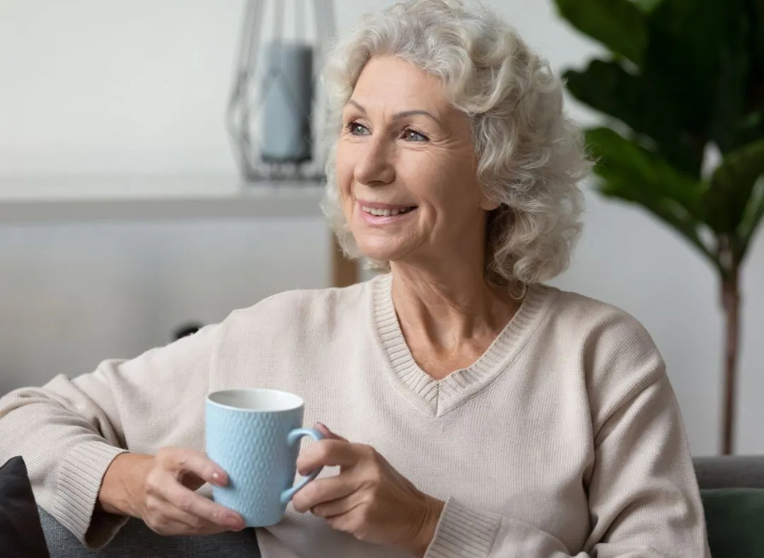 Lady sitting on sofa drinking a cup of tea or coffee smiling