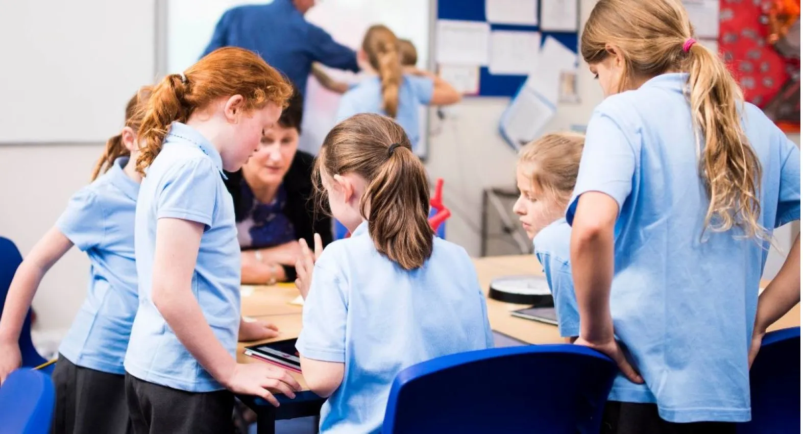 Photo of children in a classroom talking with a teacher or classroom assistant